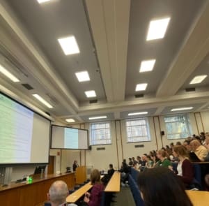 People sitting in a lecture room looking at a presenter in a podium.