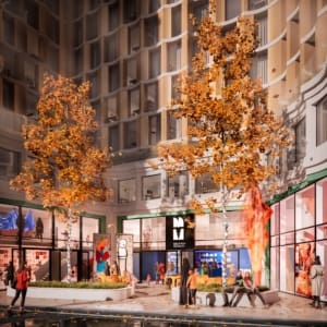 View of the entrance of a building, two trees in front with people sitting around them. Night time, with fluorescent lights on.