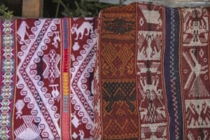 Older and more recent textiles displayed side by side show how pallay changes over time. The newer textile on the left incorporates brighter colors and more figurative motifs, while the older textile on the right uses a darker palette and denser geometric compositions.